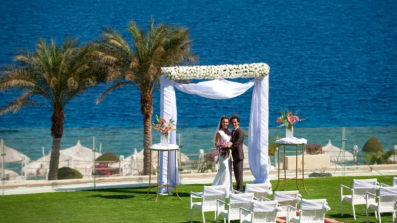 A Man And Woman Standing In Front Of A White Tent On A Beach